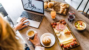 Una computadora portátil sobre una mesa con una bandeja de desayuno que contiene croissants, tomates, queso y jamón.