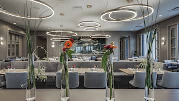 Un comedor moderno con mesas redondas, jarrones transparentes con flores y luces de techo circulares.