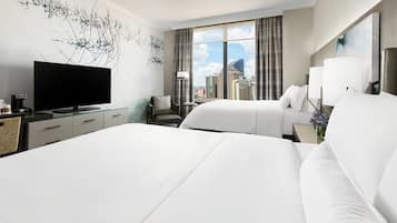 A hotel room with a large bed, a flat-screen TV, a desk with a computer, and a window with a city view.