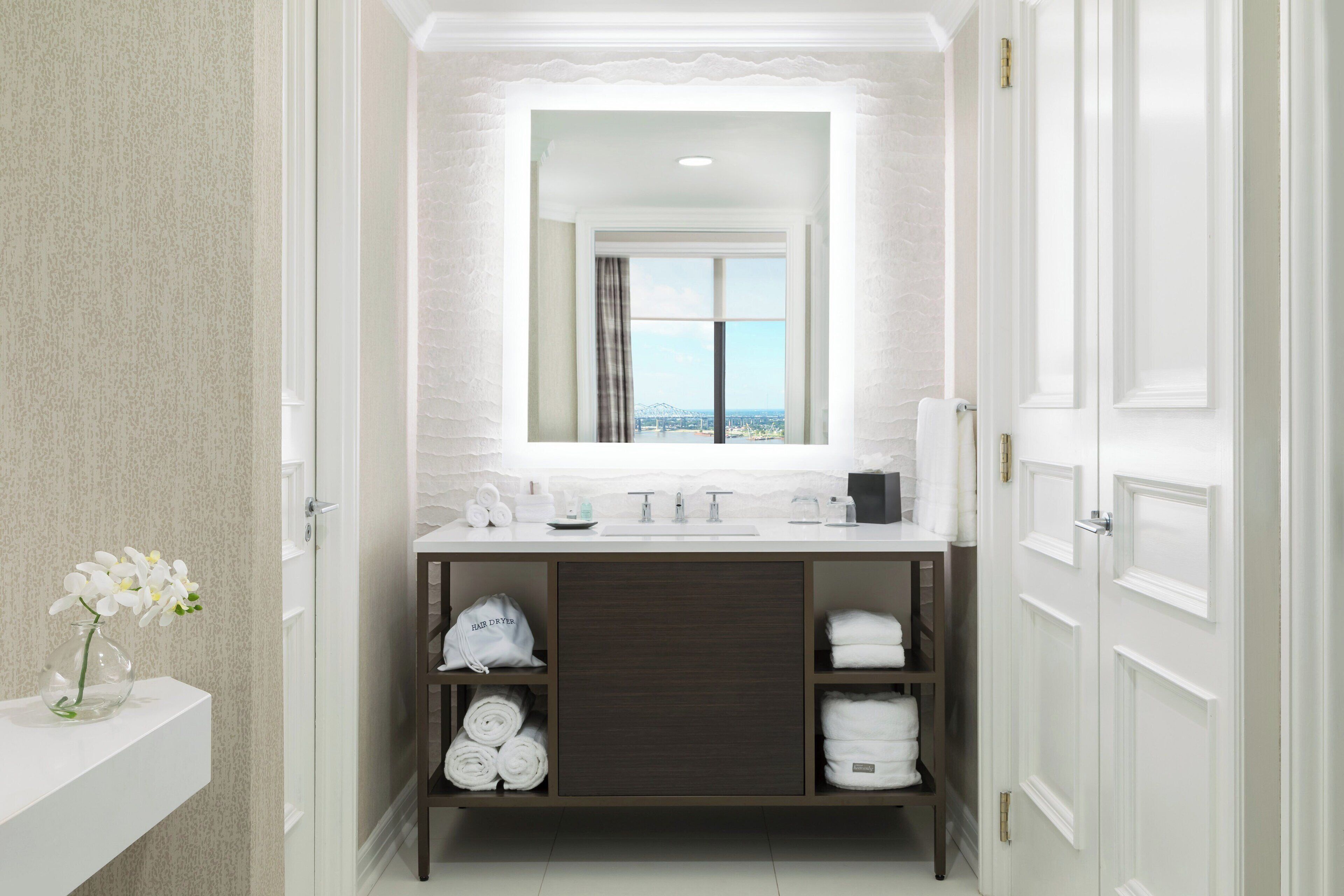 A modern bathroom with a large mirror, a white sink, and a view of the city through the window.