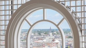 A view through a large arched window with a grid pattern, overlooking a cityscape with various buildings and a prominent church spire. - The Westin New Orleans (New Orleans)