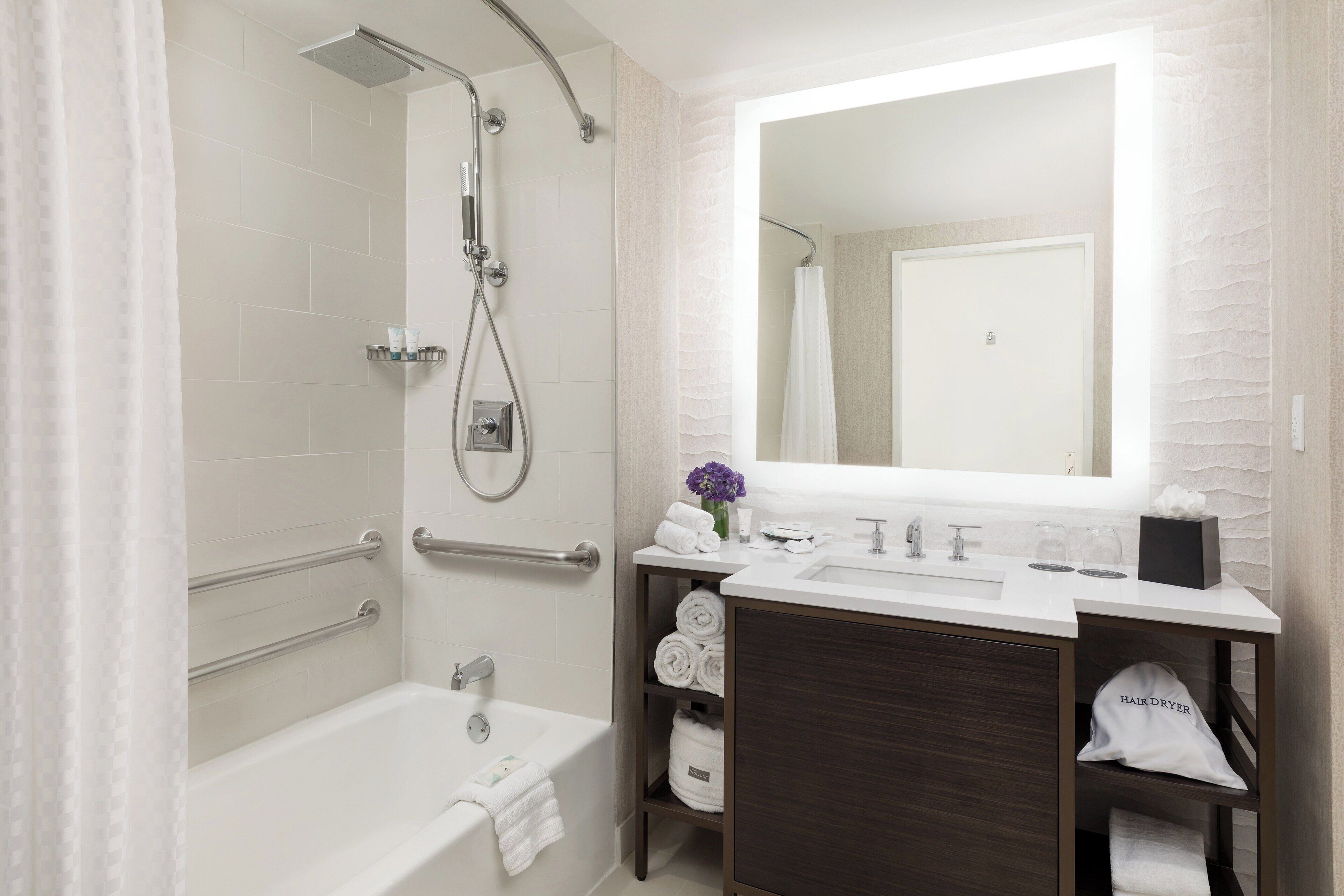 A modern bathroom with a bathtub, shower, vanity, and a large mirror.