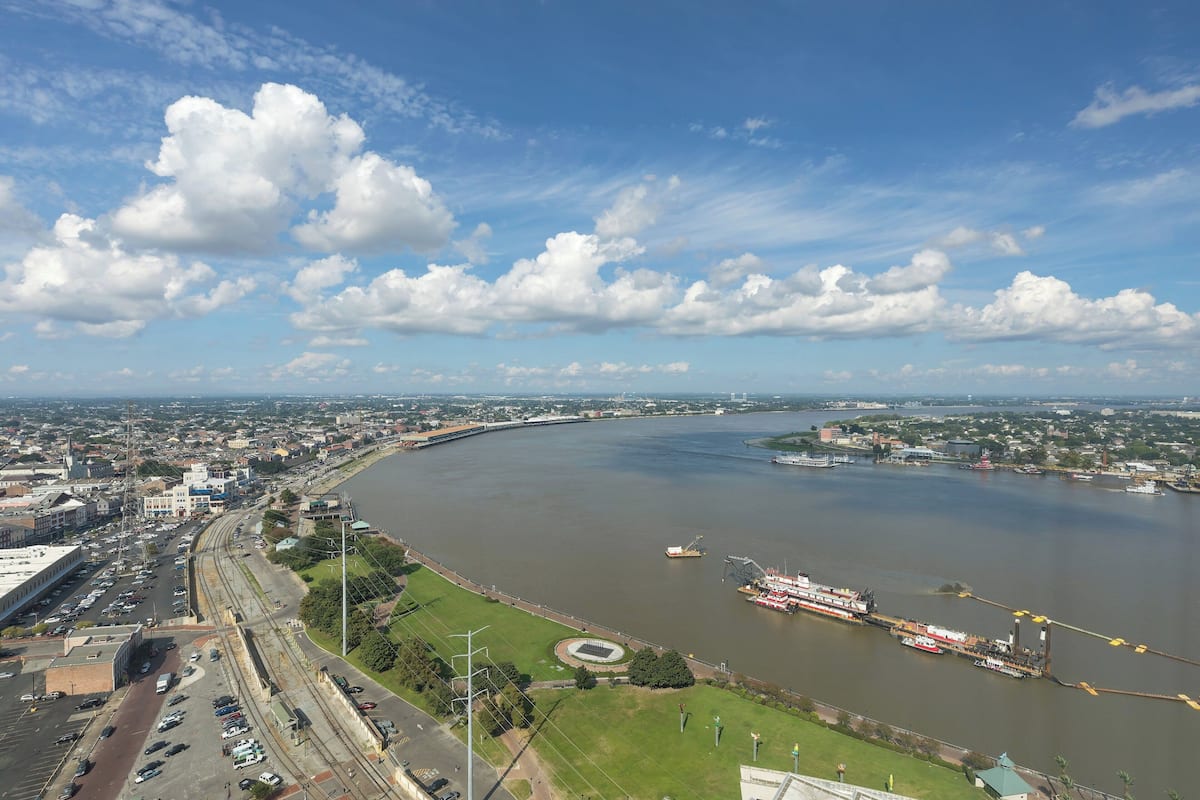 An aerial view of a river with a bridge, a boat, and a cityscape with buildings and greenery.
