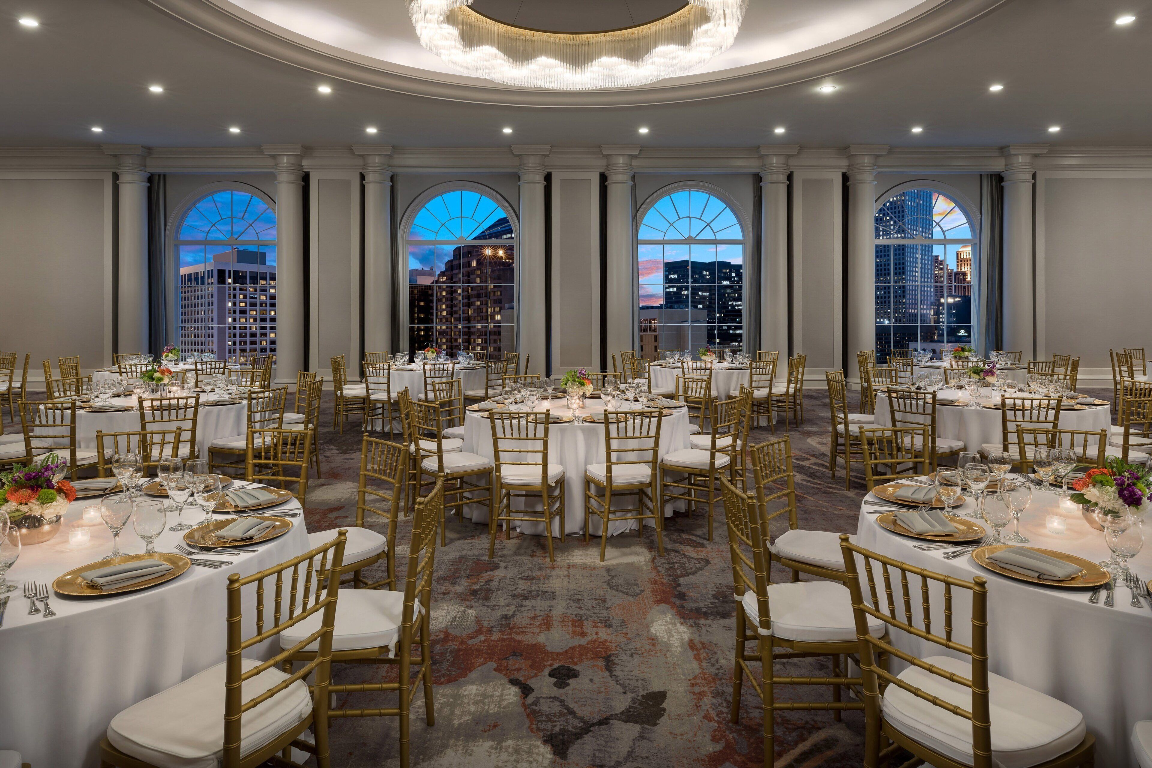 A banquet hall with round tables, gold chairs, and white tablecloths.