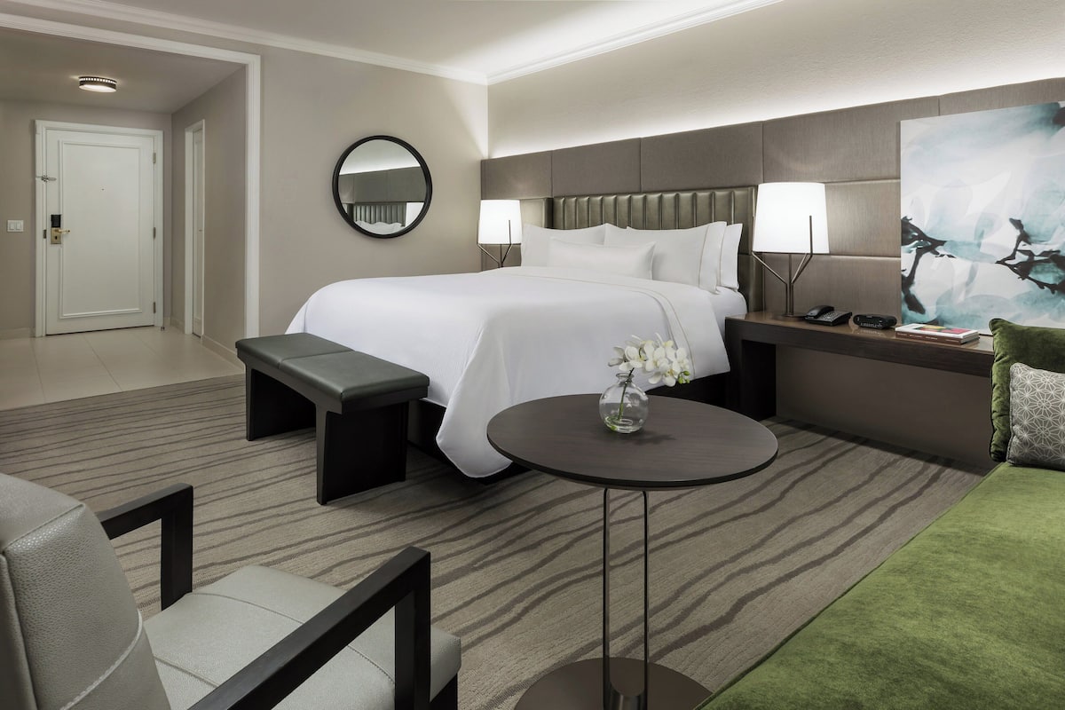 A hotel room with a large bed, bedside tables, a round table, and a green sofa.
