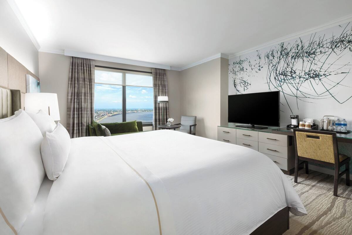 A hotel room with a large bed, a desk with a chair, a television, and a view of the city.