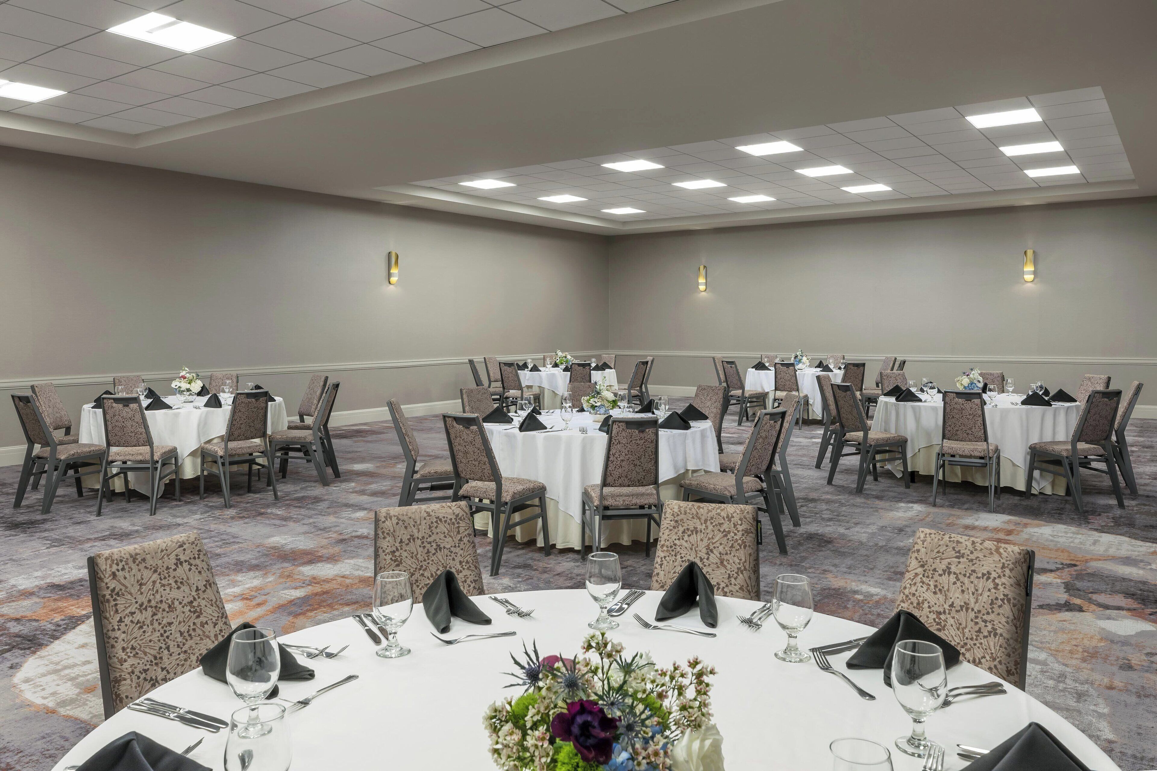 Un salón de conferencias con mesas redondas, sillas y centros de mesa florales.