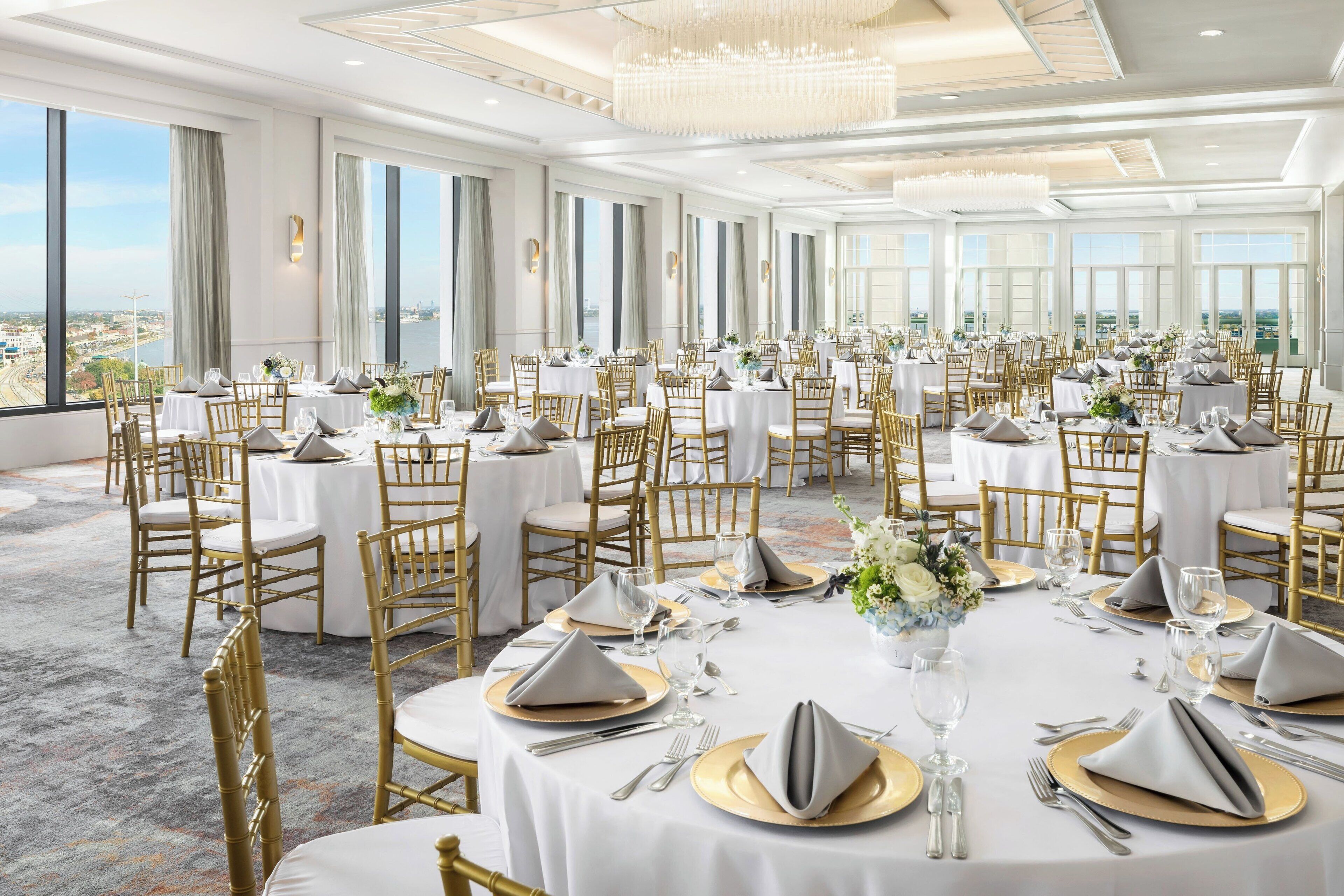 A banquet hall with round tables set for dining, large windows, and a view of the city.