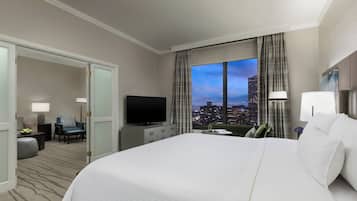 Habitación de hotel con una cama grande, televisión, escritorio con silla y vista nocturna de la ciudad.