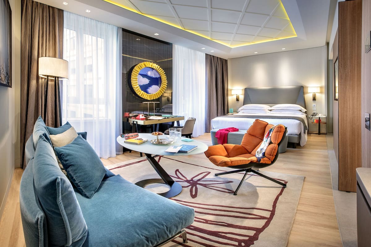 Moderni hotellihuone, jossa on suuri sänky, sohva, työpöytä ja ruokapöytä.
