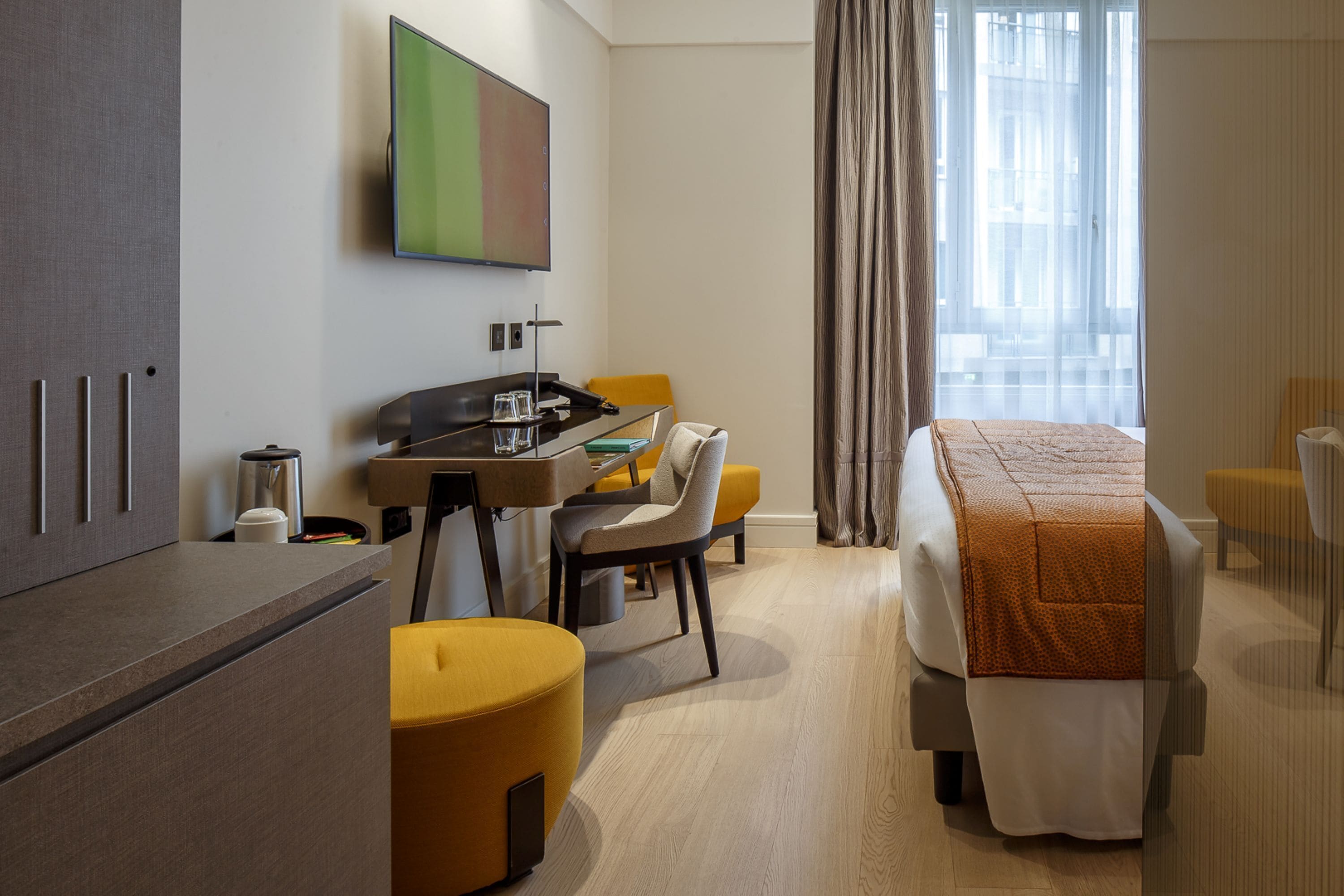A hotel room with a bed, a desk with a chair, a television, and a window with curtains.