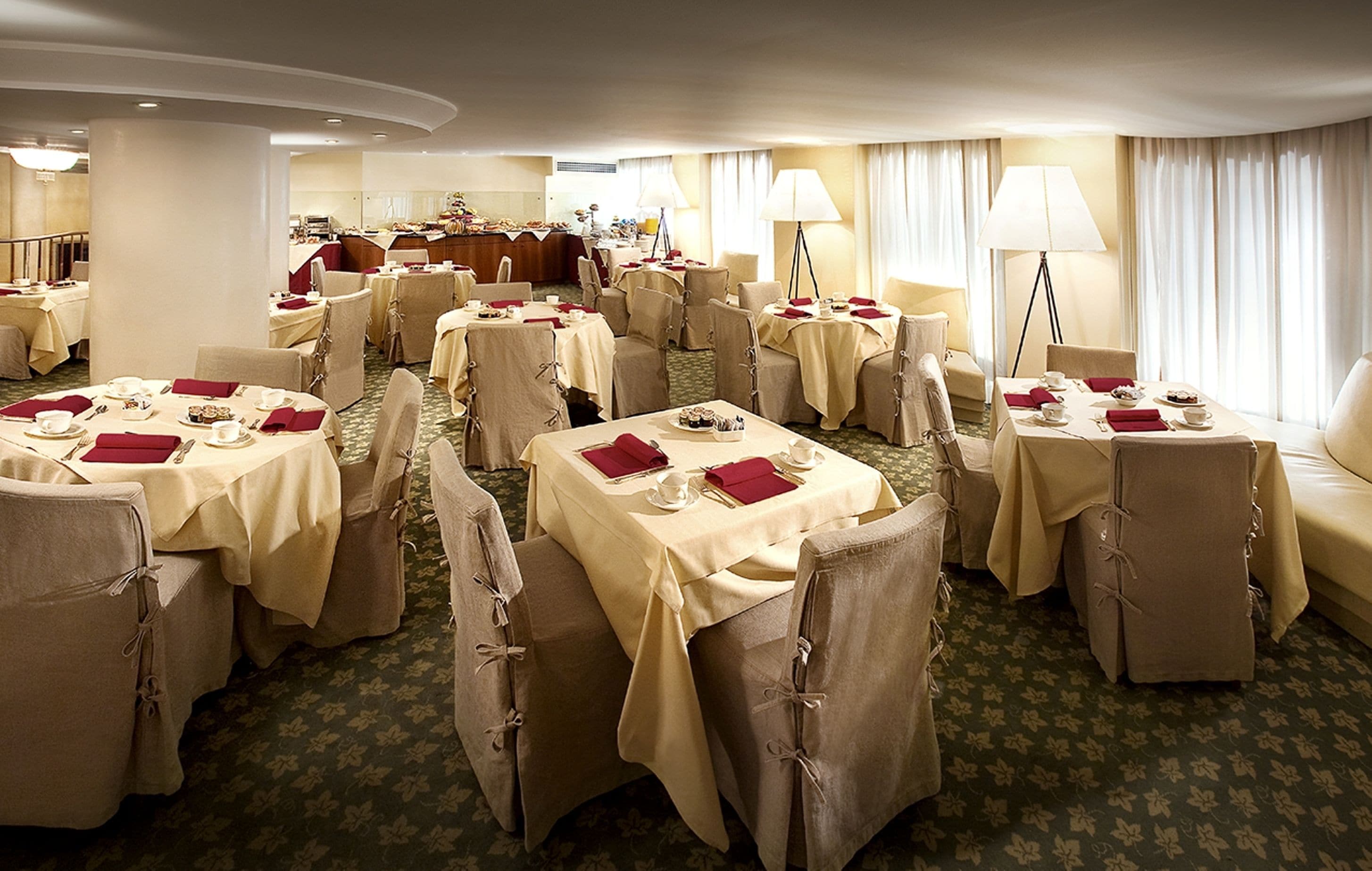 En hotelrestaurant med flere borde dækket til spisning, alle med stole og service.