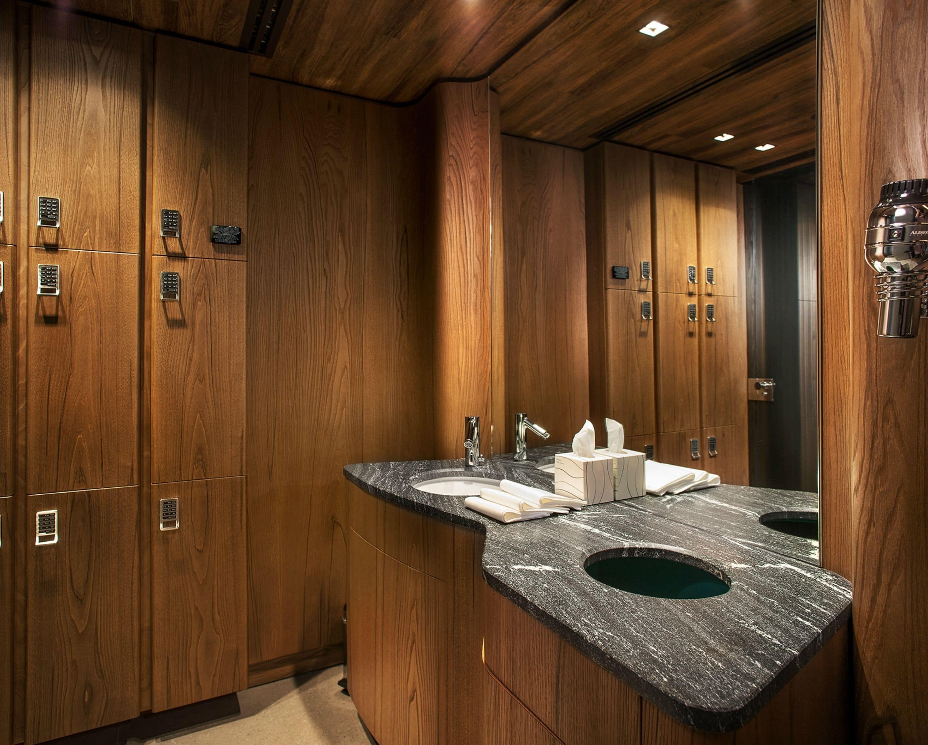 A modern bathroom with wooden cabinetry, a marble countertop, and a large mirror.
