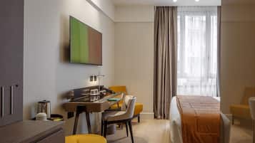 Una camera d'albergo con un letto, una scrivania con una sedia, una macchina per il caffè e un televisore appeso al muro.
