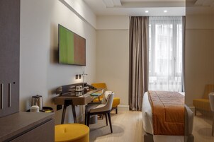 A hotel room with a bed, a desk with a chair, a coffee machine, and a television on the wall.