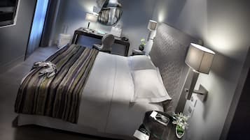 Een moderne hotelkamer met een opgemaakt bed, een bureau met stoel, een nachtkastje met lamp, en een grote spiegel aan de muur.