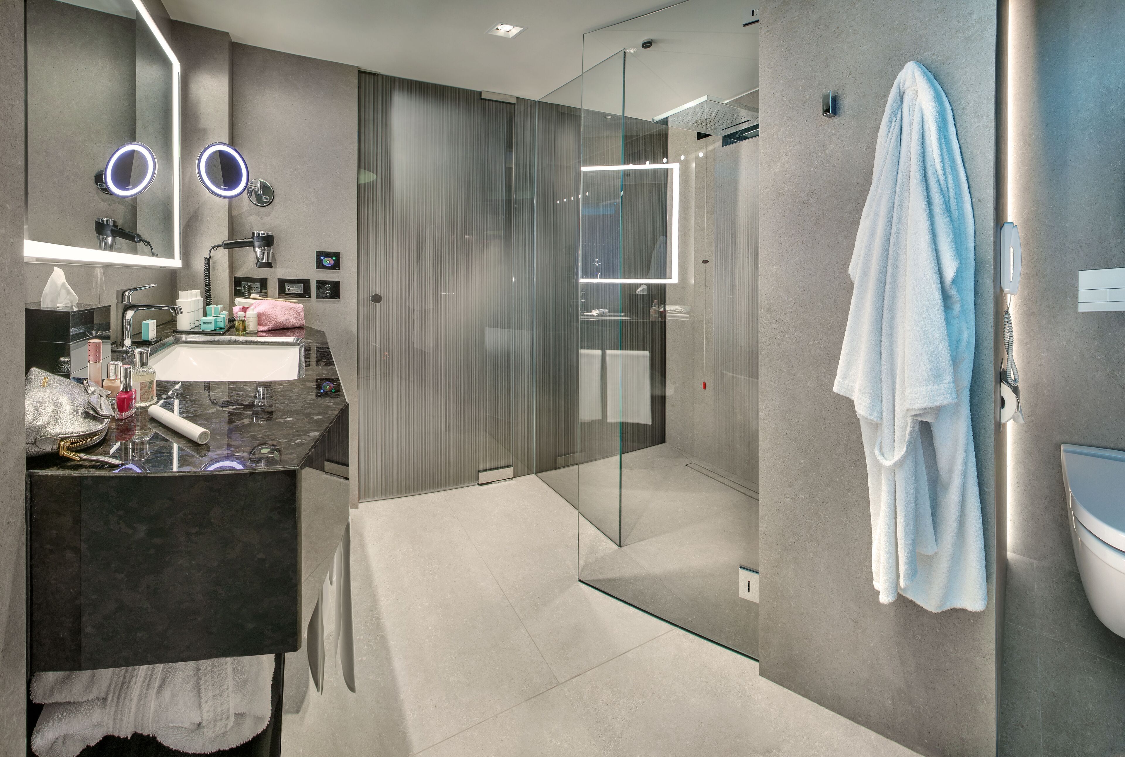 Une salle de bain moderne avec une douche à l’italienne, un meuble-lavabo doté d’un plan de toilette foncé et une serviette accrochée au mur.