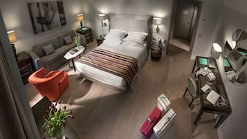Une chambre d’hôtel moderne, dotée d’un grand lit, d’un canapé, d’un bureau et d’une chaise. On y trouve deux tables de chevet avec des lampes, ainsi qu’une petite table sur laquelle est posé un vase de fleurs.