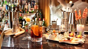 A bar with a variety of drinks, including a martini and a cocktail with an orange slice. There are also shrimp skewers and appetizers on the table. - Hotel Cavour (Milan)
