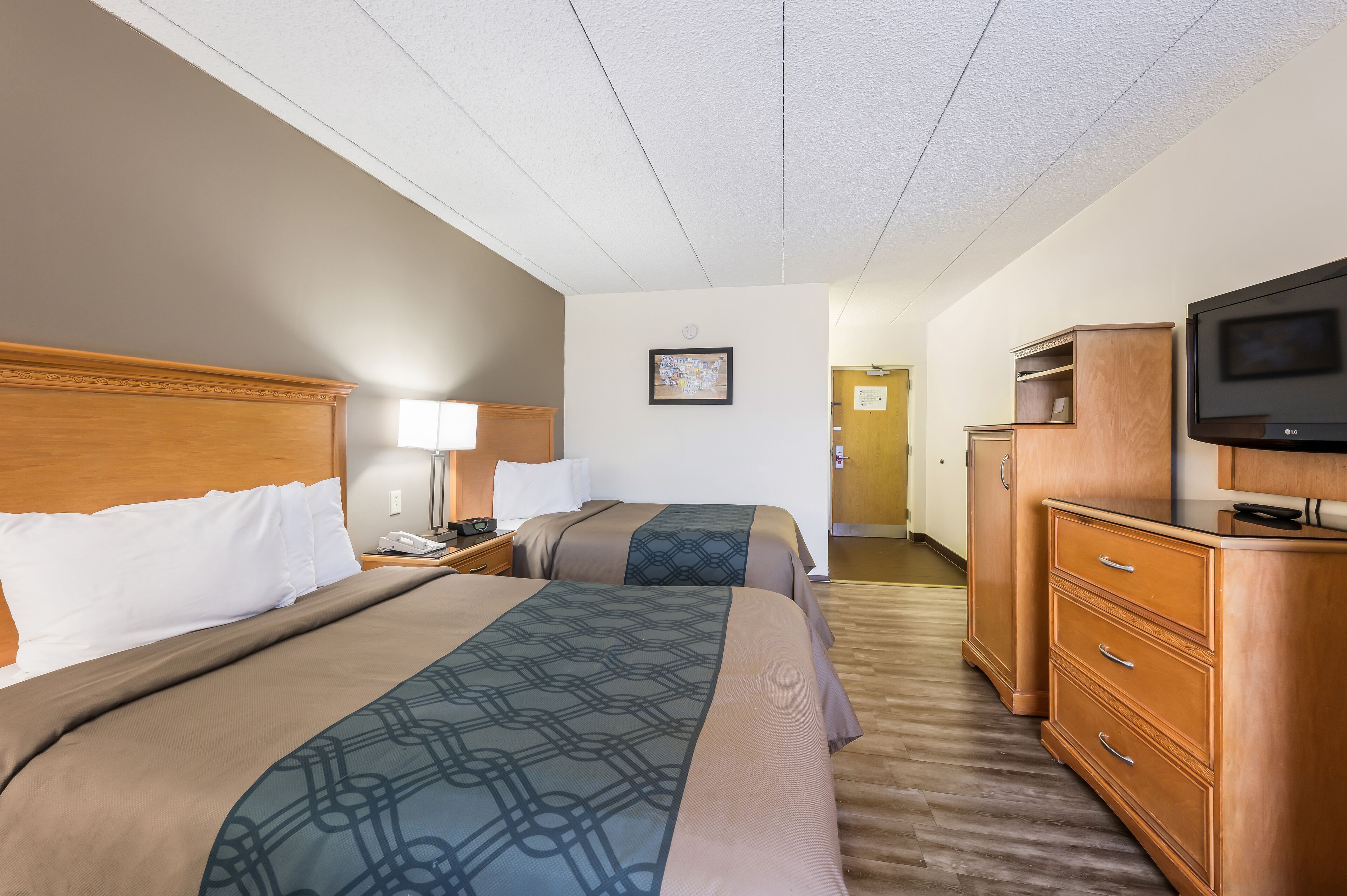 A hotel room with two beds, wooden headboards, a TV, a desk with a lamp, and a wardrobe.