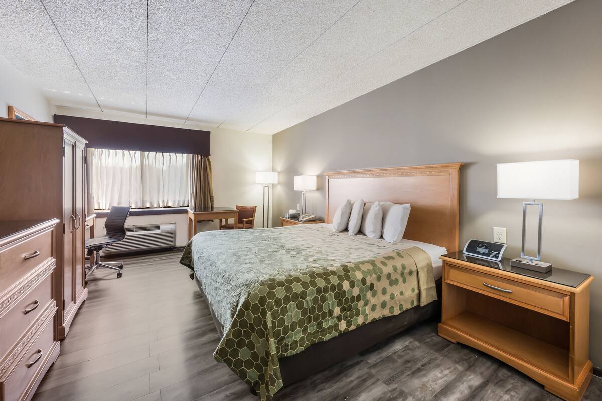 Une chambre d’hôtel avec un grand lit, un bureau, une chaise, une armoire et une table de chevet avec une lampe.