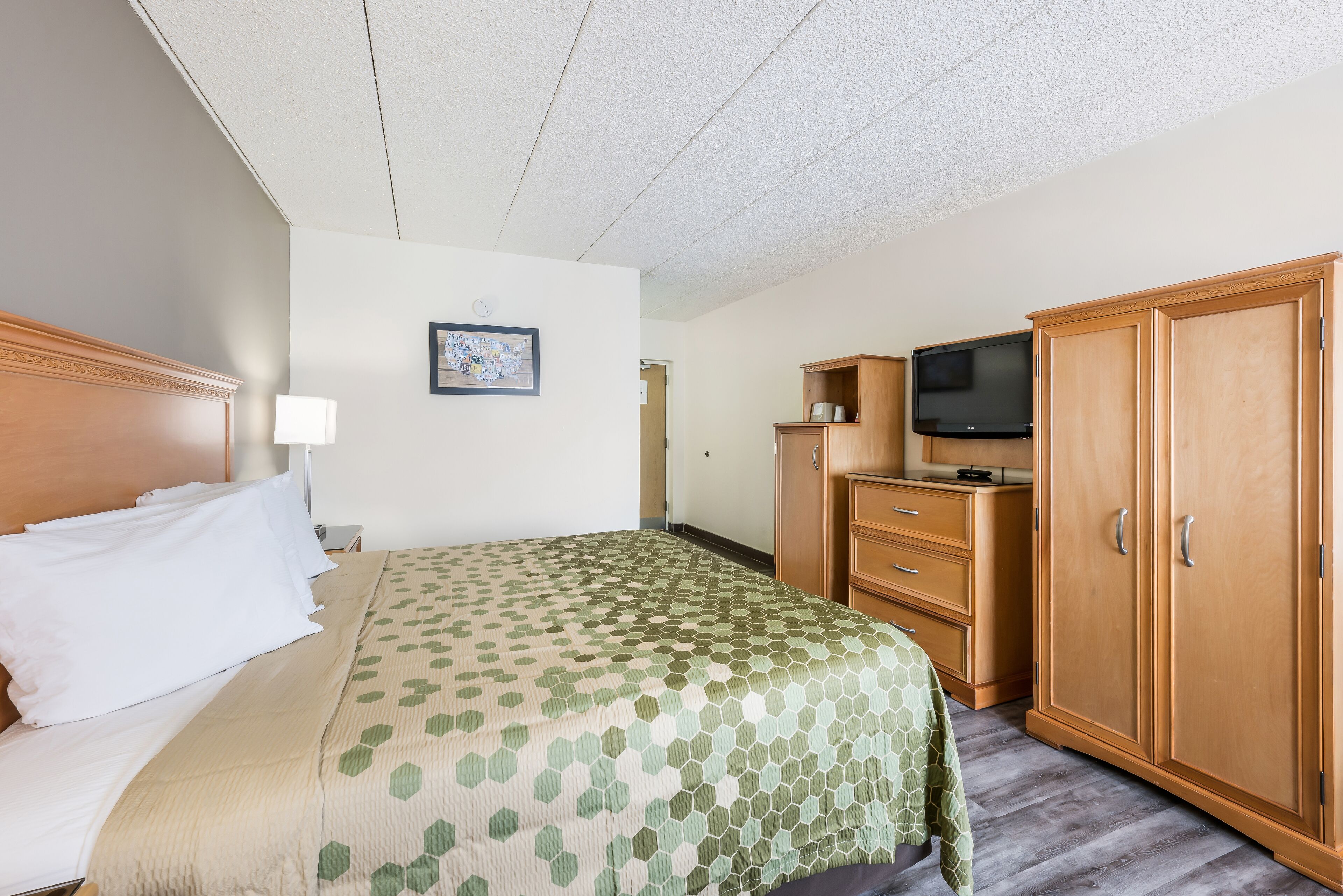A hotel room with a bed, a television, wooden cabinets, and a framed picture on the wall.