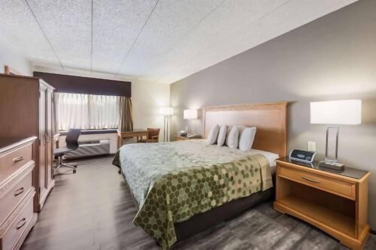 Une chambre d’hôtel comprenant un lit, une table de chevet, une lampe, un bureau, une chaise et une armoire.