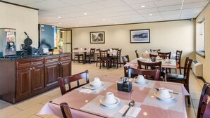 Comedor de hotel con varias mesas y sillas, una barra de cocina con electrodomésticos y cuadros en las paredes.