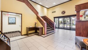 Vestíbulo de hotel con una escalera de madera, una recepción y un amplio escaparate de vidrio que da al exterior.