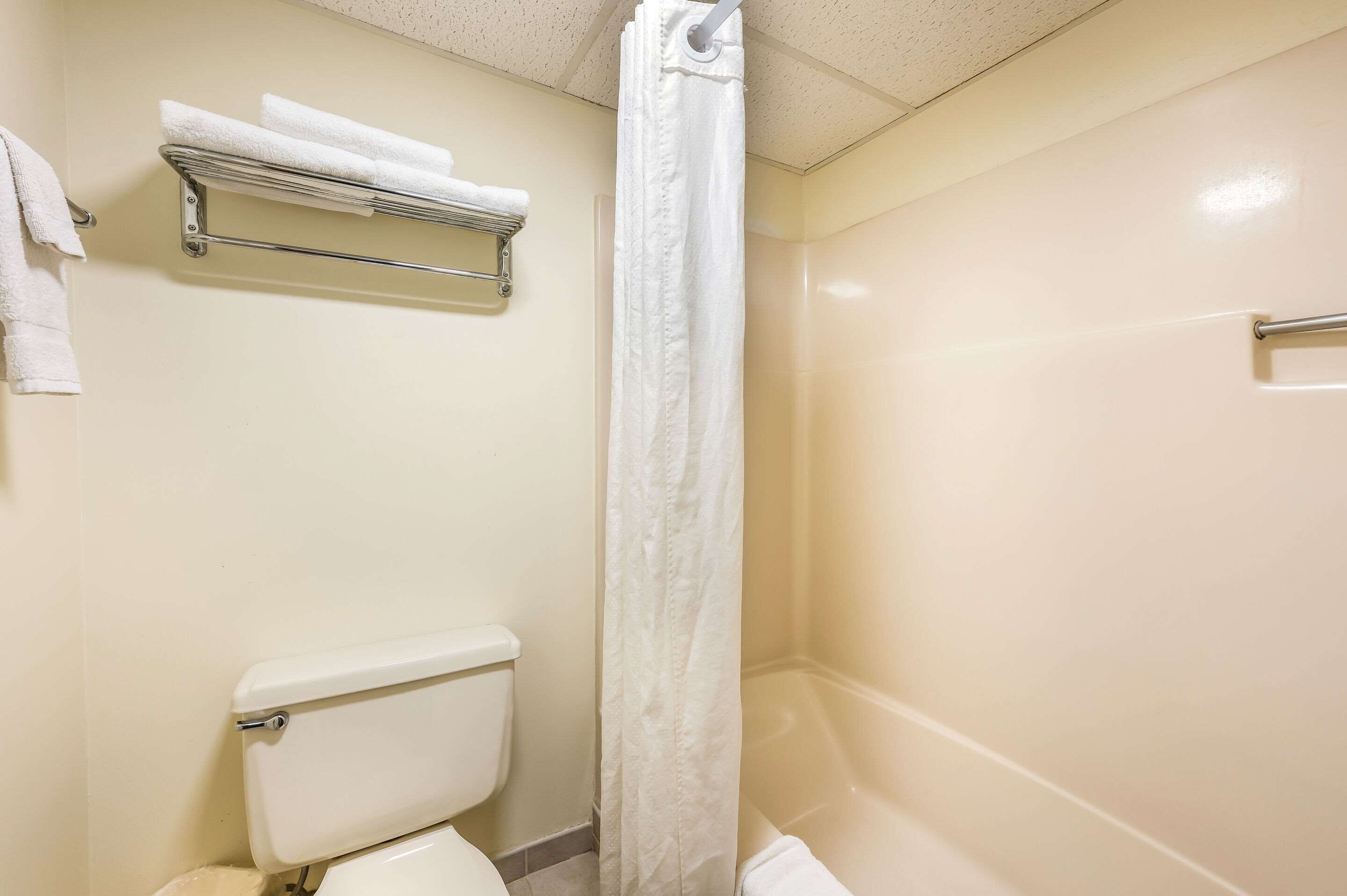 A bathroom with a toilet, a shower with a curtain, and a towel rack with towels.