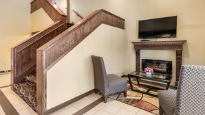 Una escalera con barandillas de madera, un televisor de pantalla plana sobre una chimenea, y dos sillones estampados en una sala de estar.