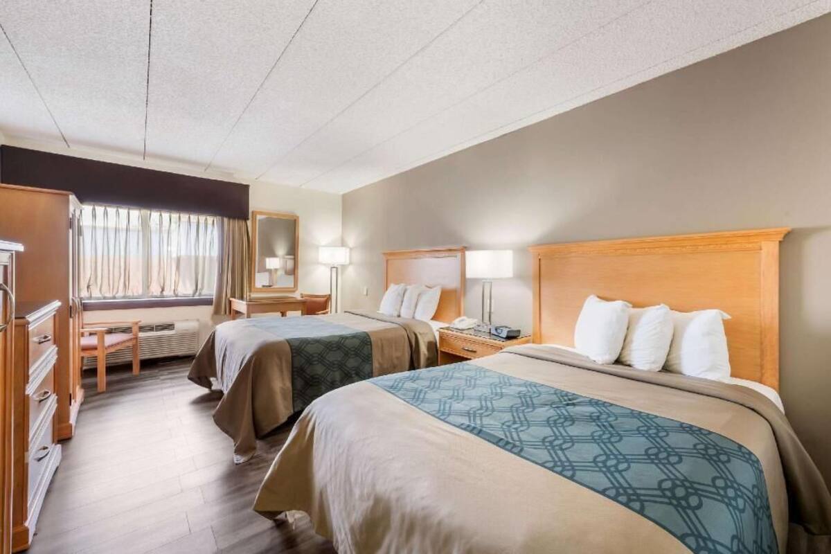 Une chambre d’hôtel avec deux lits, un bureau, une chaise, une fenêtre avec des rideaux et un miroir.