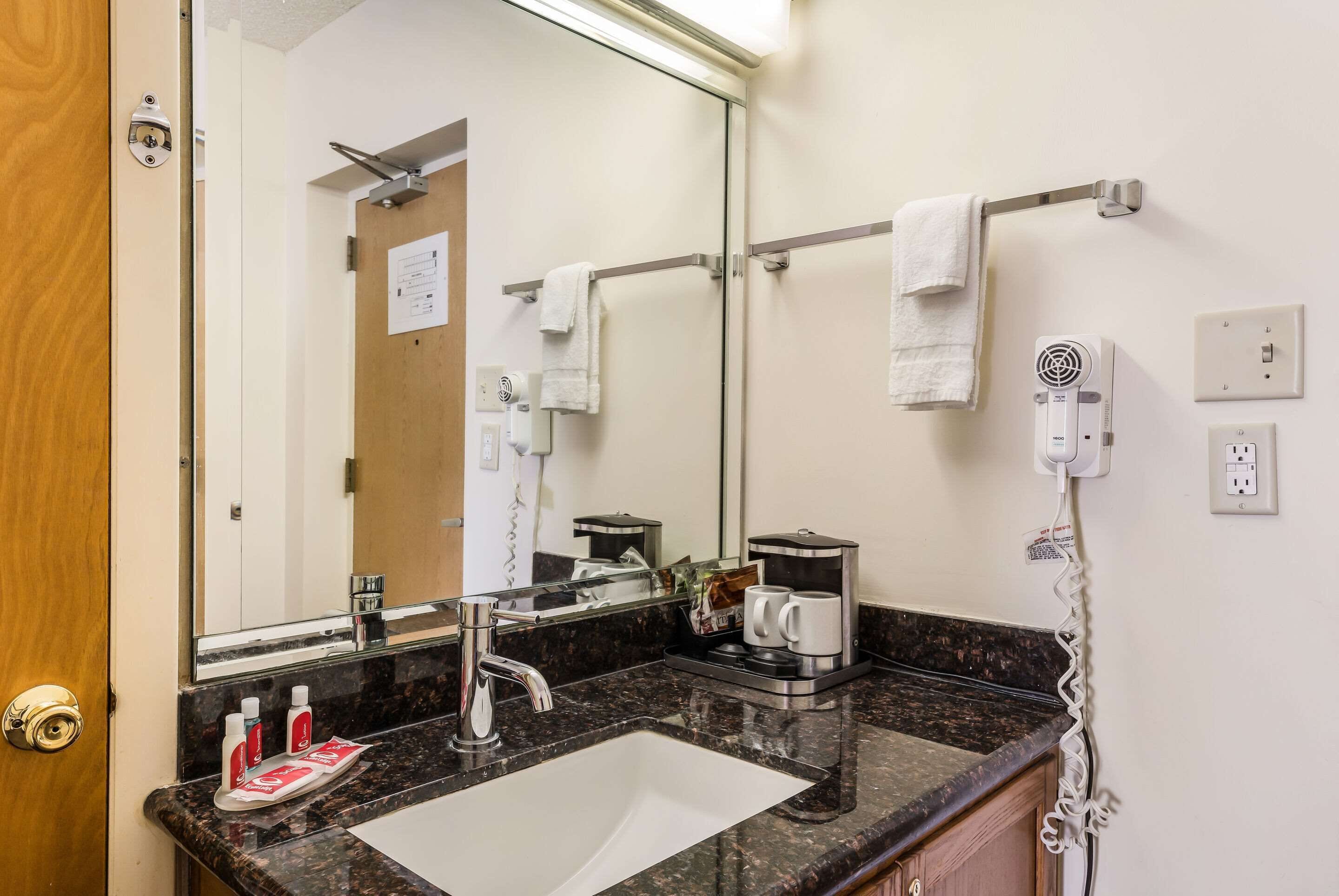 Une salle de bain d’hôtel équipée d’un lavabo, d’un miroir, d’un porte-serviettes et d’un sèche-cheveux fixé au mur.