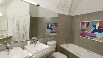 Ein modernes Badezimmer mit zwei Waschbecken, einer Toilette und einer Badewanne. Auf der Ablagefläche liegen Handtücher und Toilettenartikel.