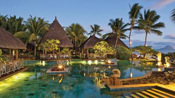 Relax by the serene pool surrounded by palm trees and thatched-roof structures.