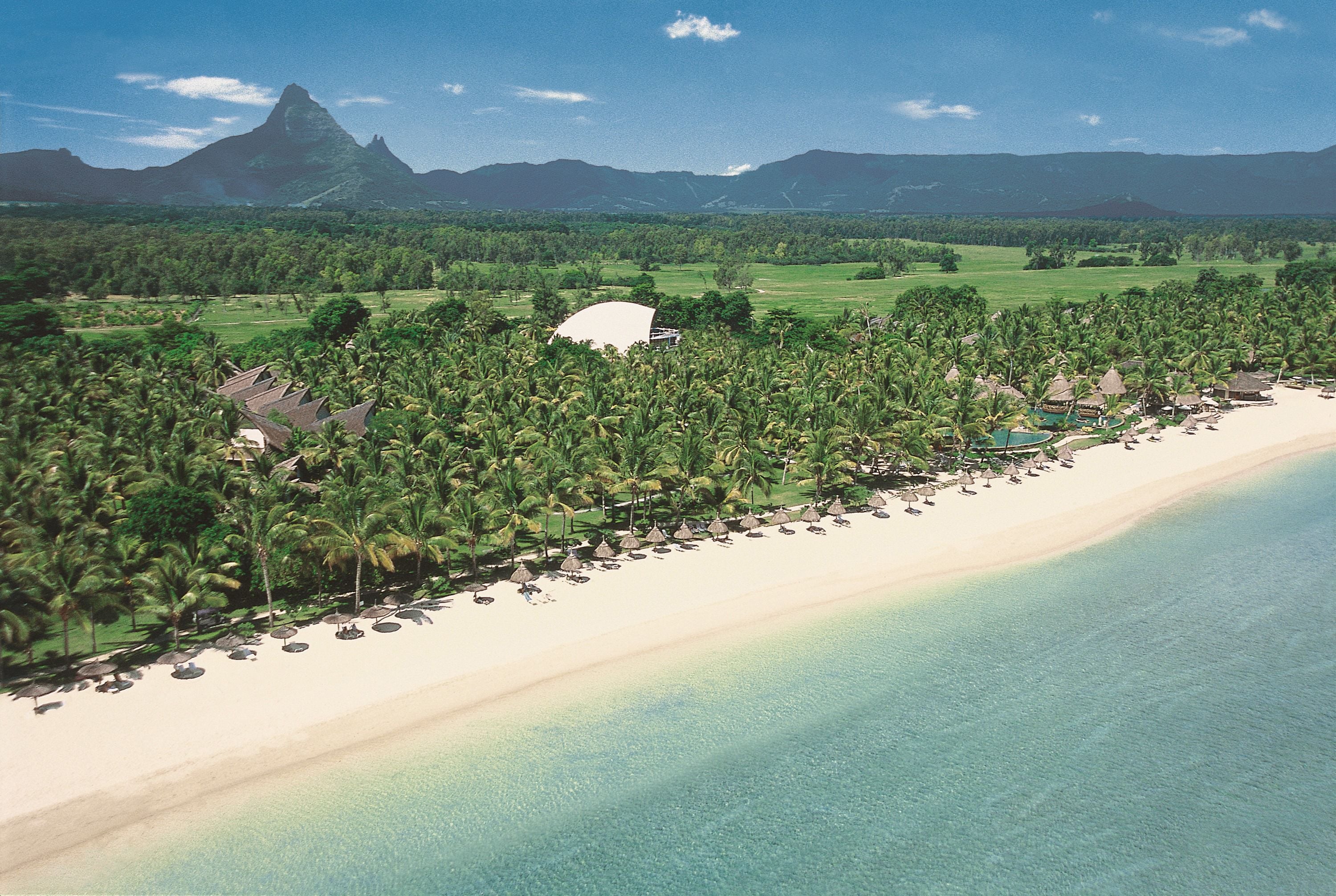 A beach resort with a long stretch of beach, palm trees, and a mountain in the background.