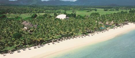 A beach resort with a long stretch of beach, palm trees, and a mountain in the background.
