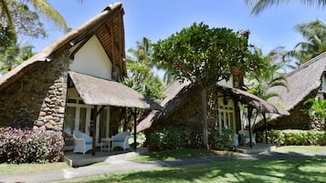 Um resort com chalés de telhado de palha, paredes de pedra e vegetação exuberante.