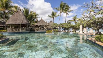 A clear pool with thatched-roof structures, palm trees, and a clear sky.