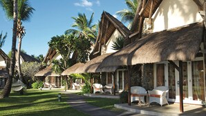 A resort with thatched-roof cottages, outdoor seating, and lush greenery. - La Pirogue Mauritius (Flic-en-Flac)