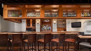A bar area with wooden shelves displaying bottles, a stone wall, and a television mounted above the bar. - Holiday Inn Houston Intercontinental Airport by IHG (Houston)