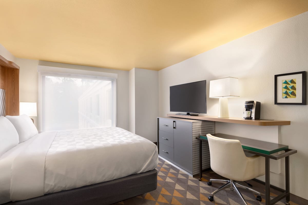 Ein Hotelzimmer mit einem Bett, einem Schreibtisch mit Computer, einem Fernseher und einem Sessel.