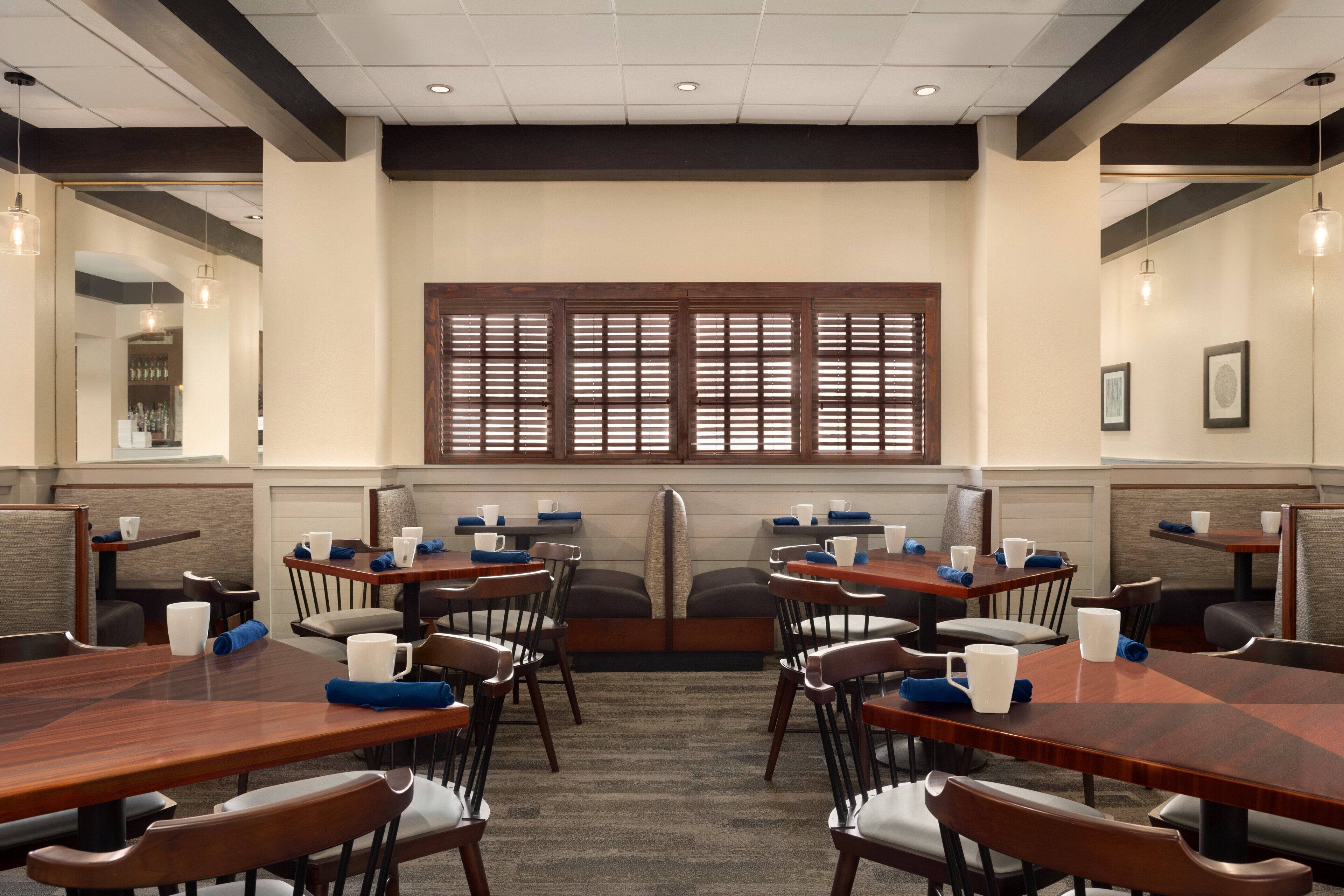 A conference room with wooden tables and chairs, a large window with blinds, and a carpeted floor.