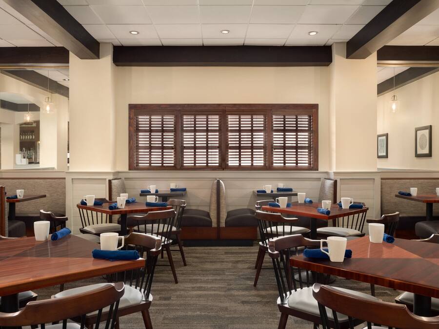 A conference room with wooden tables and chairs, a large window with blinds, and a carpeted floor.