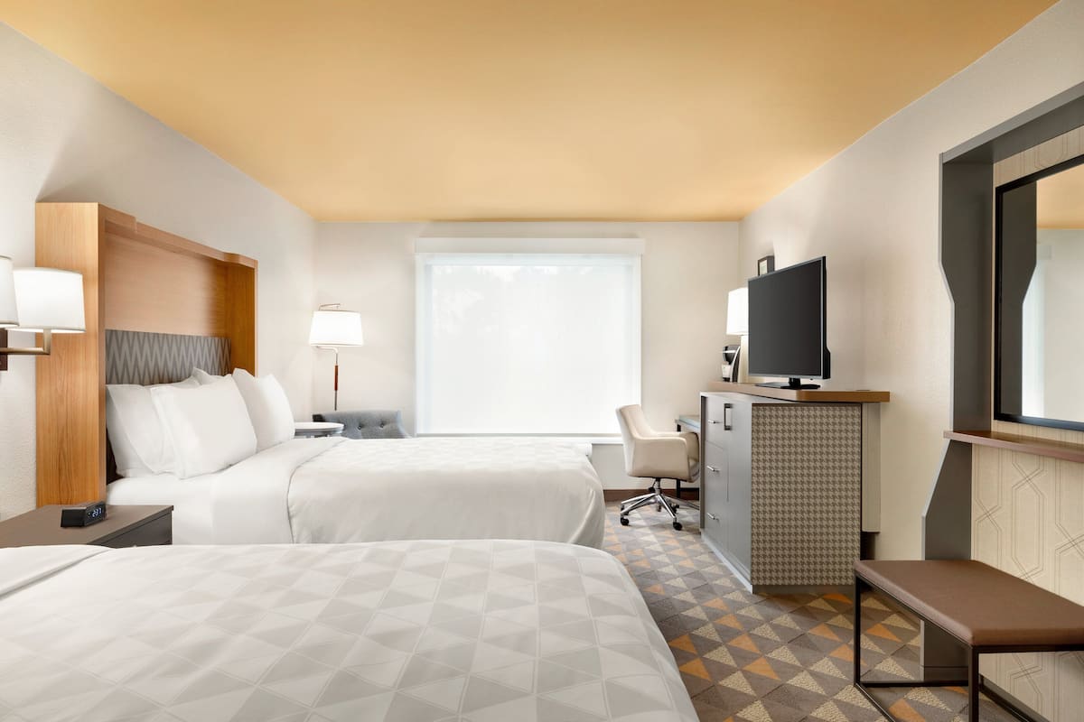 Ein Hotelzimmer mit zwei Betten, einem Schreibtisch, einem Fernseher und einem großen Fenster.