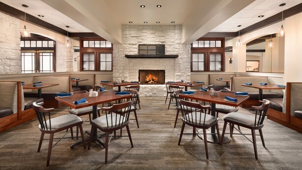 A spacious dining area with high ceilings, stone walls, and a central fireplace. Tables and chairs are arranged for dining. - Holiday Inn Houston Intercontinental Airport by IHG (Houston)