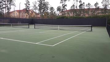 A tennis court with a net in the center, surrounded by trees and buildings.