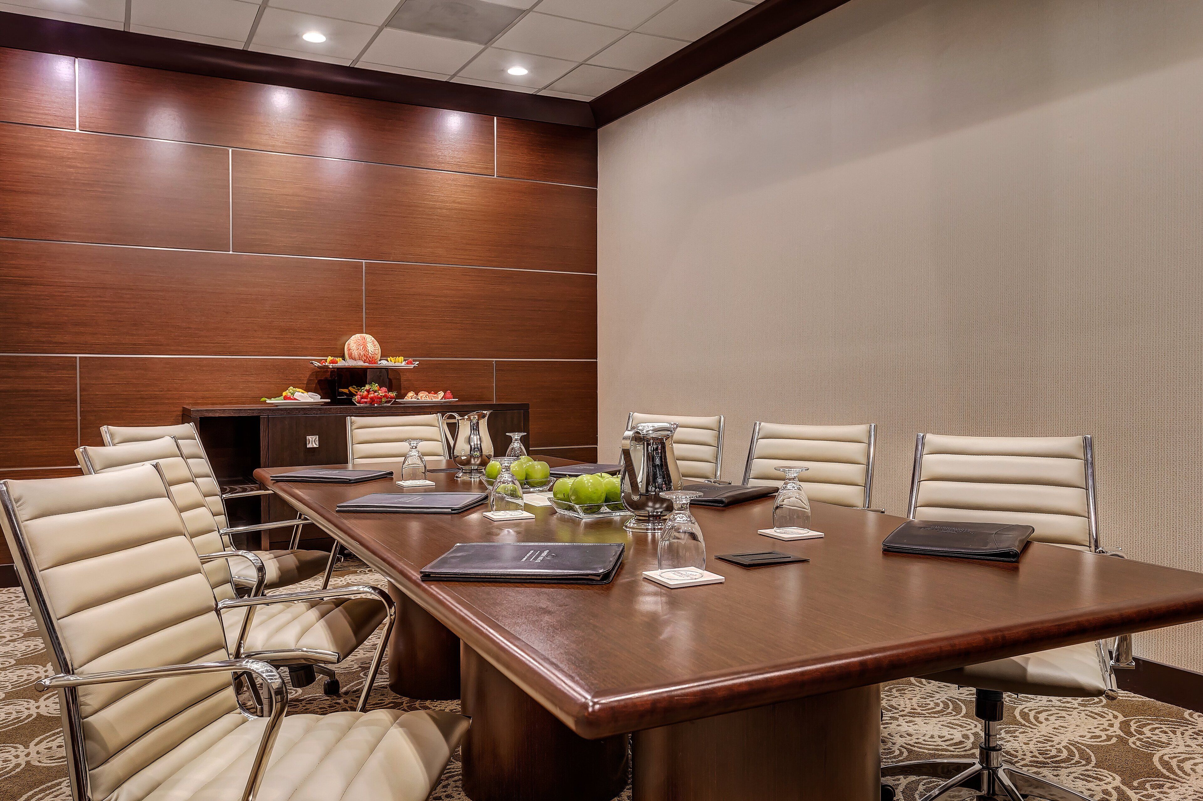 A conference room with a long table, six chairs, and a small display of fruits and a pitcher.