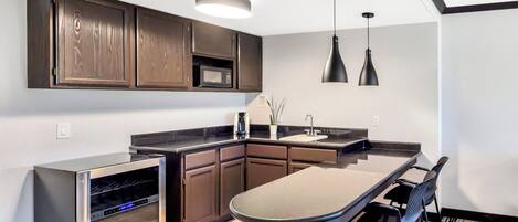 A modern kitchen with dark wooden cabinets, a stainless steel oven, a microwave, and a large island with a sink. There are two pendant lights above the island.