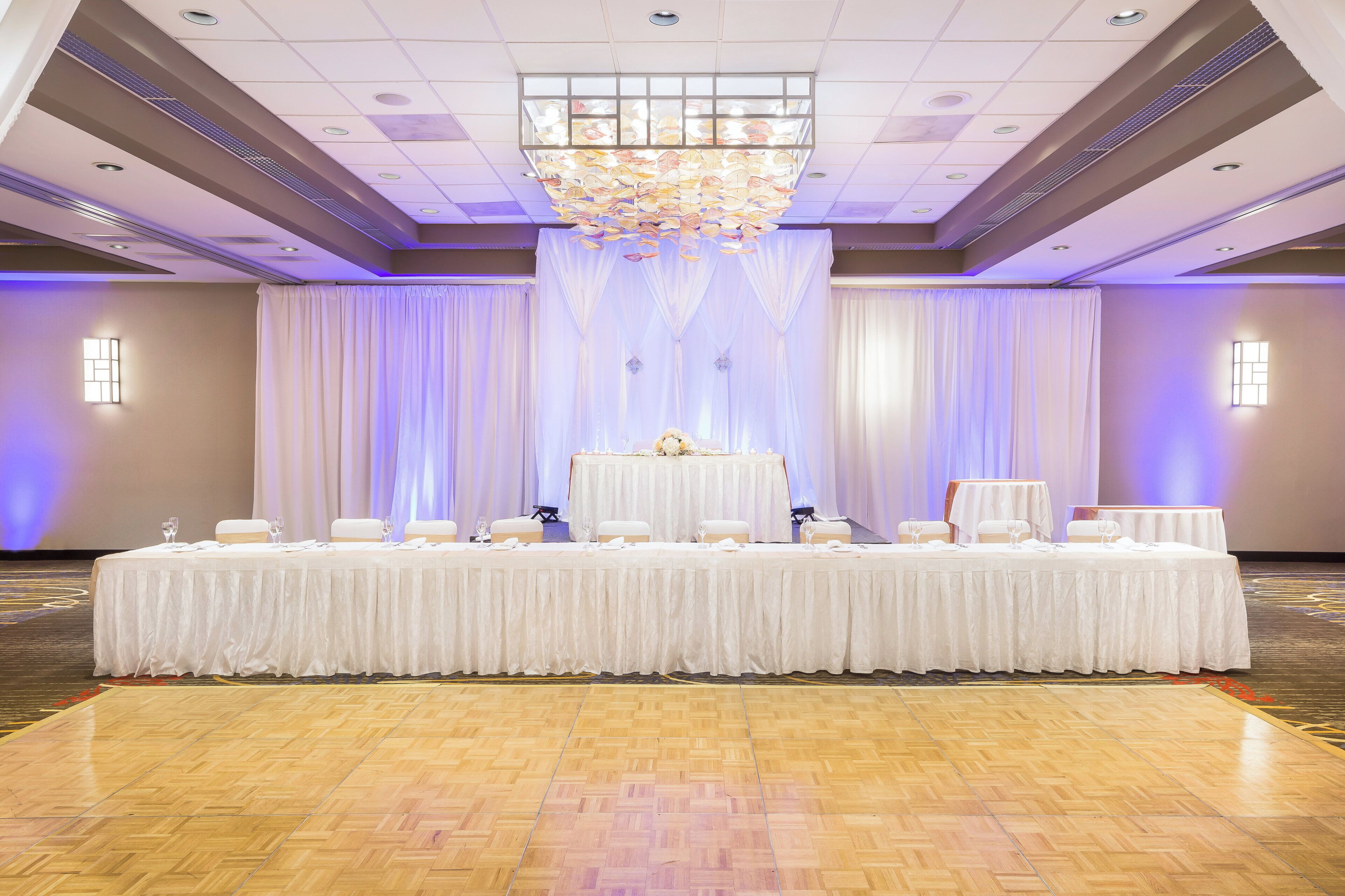 A banquet hall with a long table set for a formal event, a chandelier, and draped curtains.